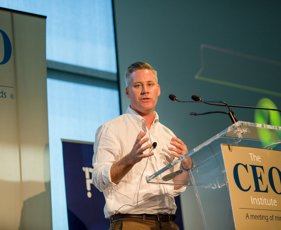 Mark Cameron gesturing mid-keynote beside a lectern